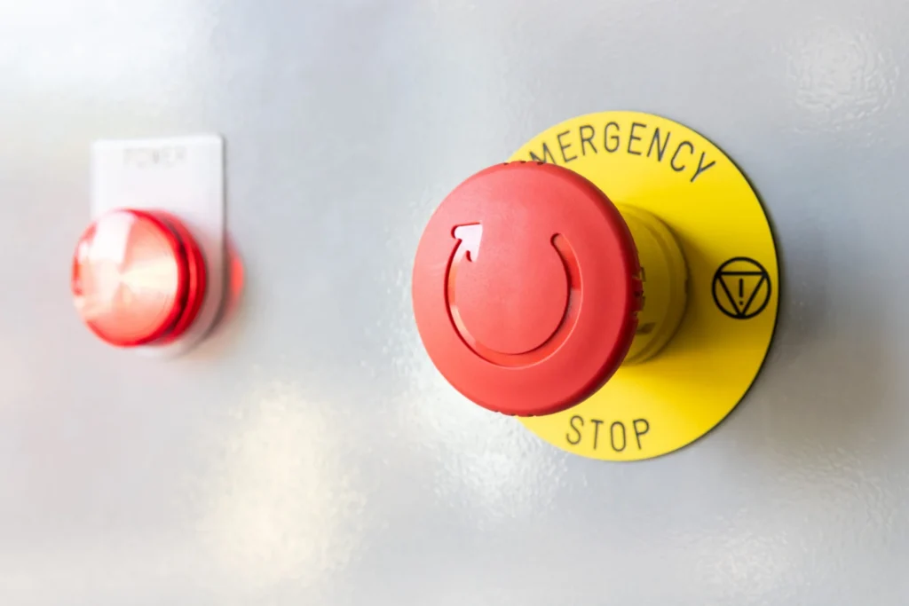 A red emergency stop button on a yellow plate.