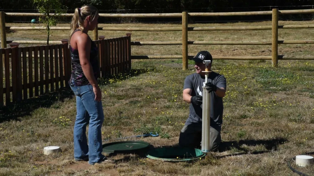 A technician kneeling at an open tank while the homeowner watches the inspection.