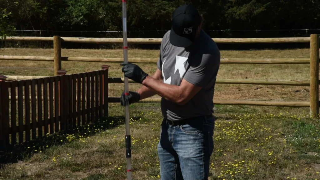 A technician measuring sludge depth with a probe pole next to the tank.