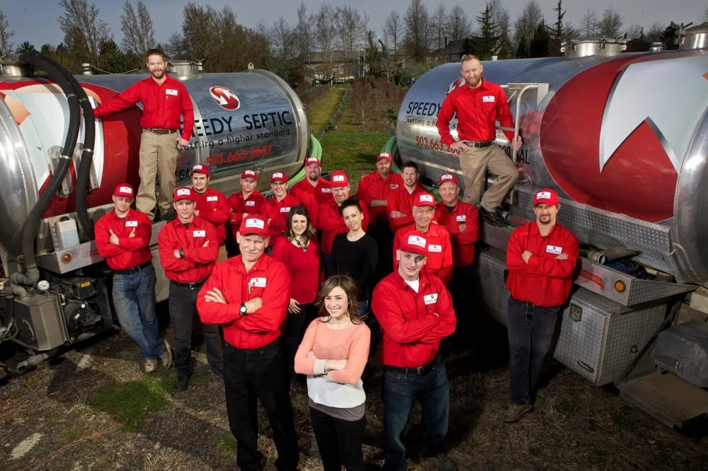 The Speedy Septic crew in red uniforms standing in front of two pump trucks.