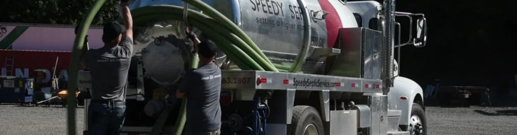 Technicians connecting hoses to a polished Speedy Septic tanker truck.
