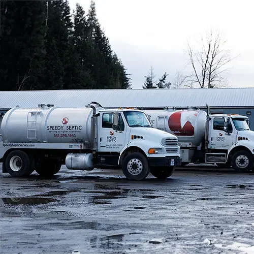 Two Speedy Septic pump trucks parked side by side on a wet morning.
